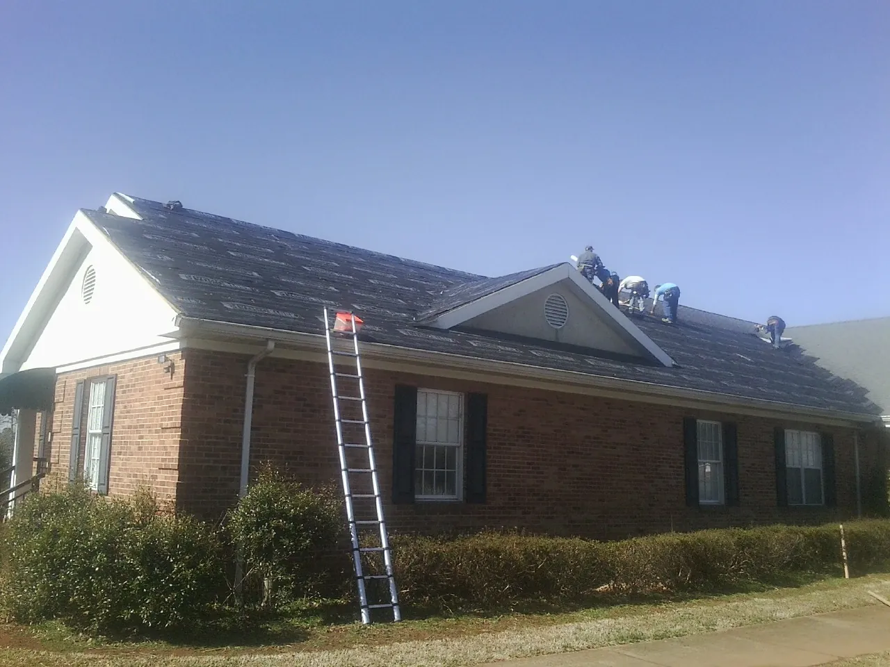 Crew tearing shingles off a brick ranch roof with a ladder set — Emergency Roof Repair work by our crew in Junction City